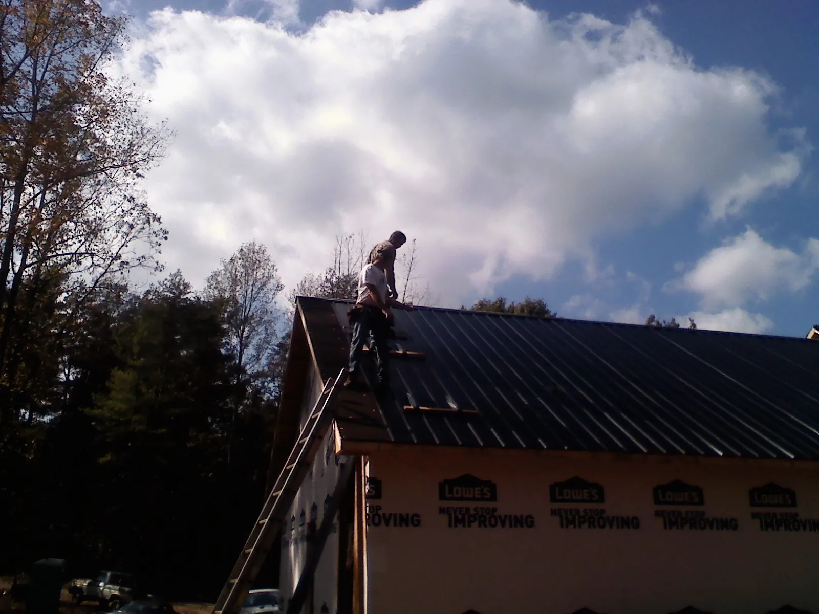 Roofer fastening dark metal panels high against a cloudy sky, from a Roof Inspection job in Neskowin