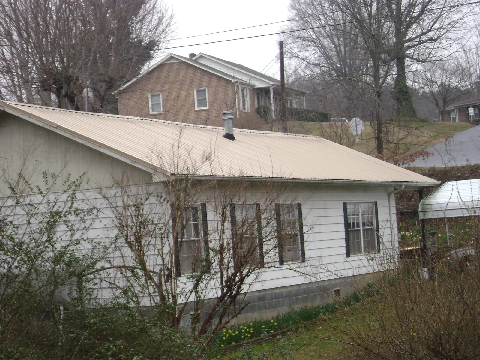 Tan metal roof on a white sided house set into a hillside — Commercial Roofing by Roofing Brothers in Neskowin